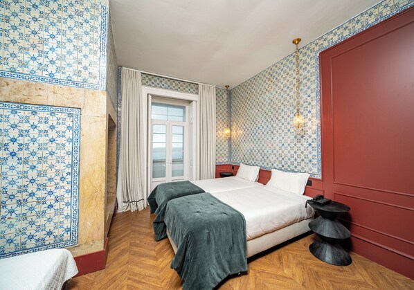 A bedroom with a large bed, two bedside tables, a window with curtains, and patterned wallpaper. - Pensão Londres (Lisbon)