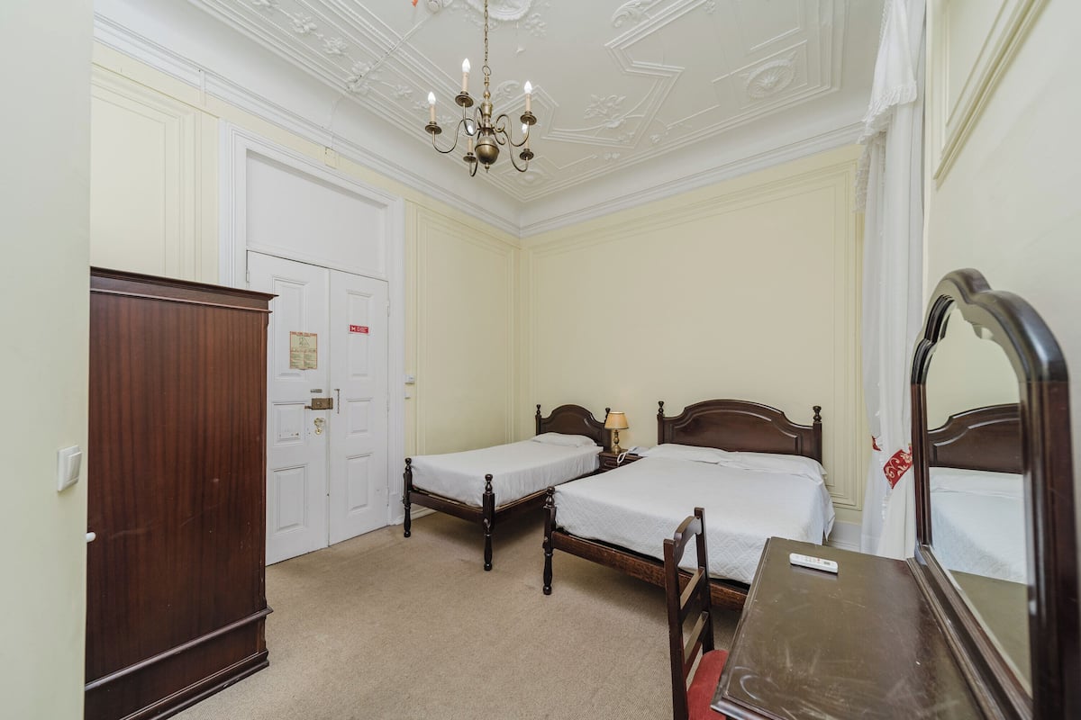 A bedroom with two single beds, a wooden wardrobe, a mirror, and a chandelier.
