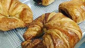 A tray of assorted pastries, including croissants and a chocolate-filled pastry, on a clear plastic tray. - Hostal Meseguer (Elche)