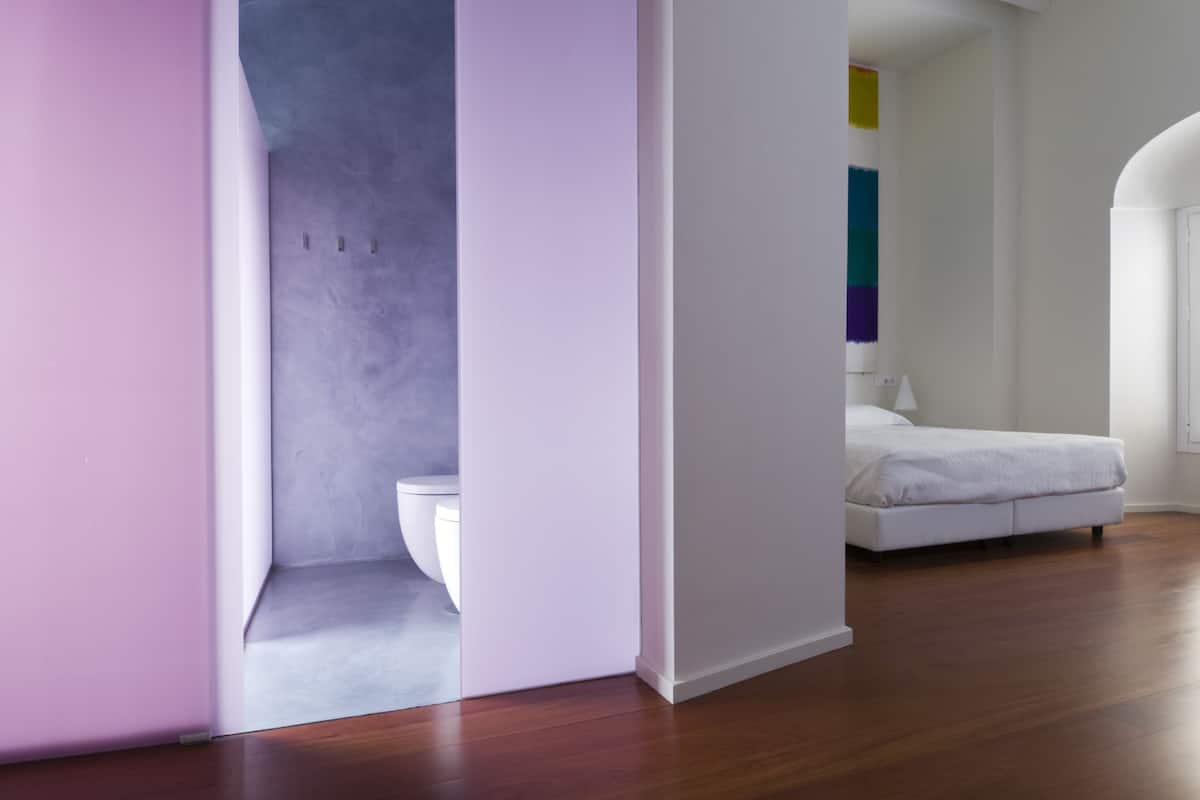 Un dormitorio moderno con una cama blanca, una mesita de noche blanca y suelo de madera.