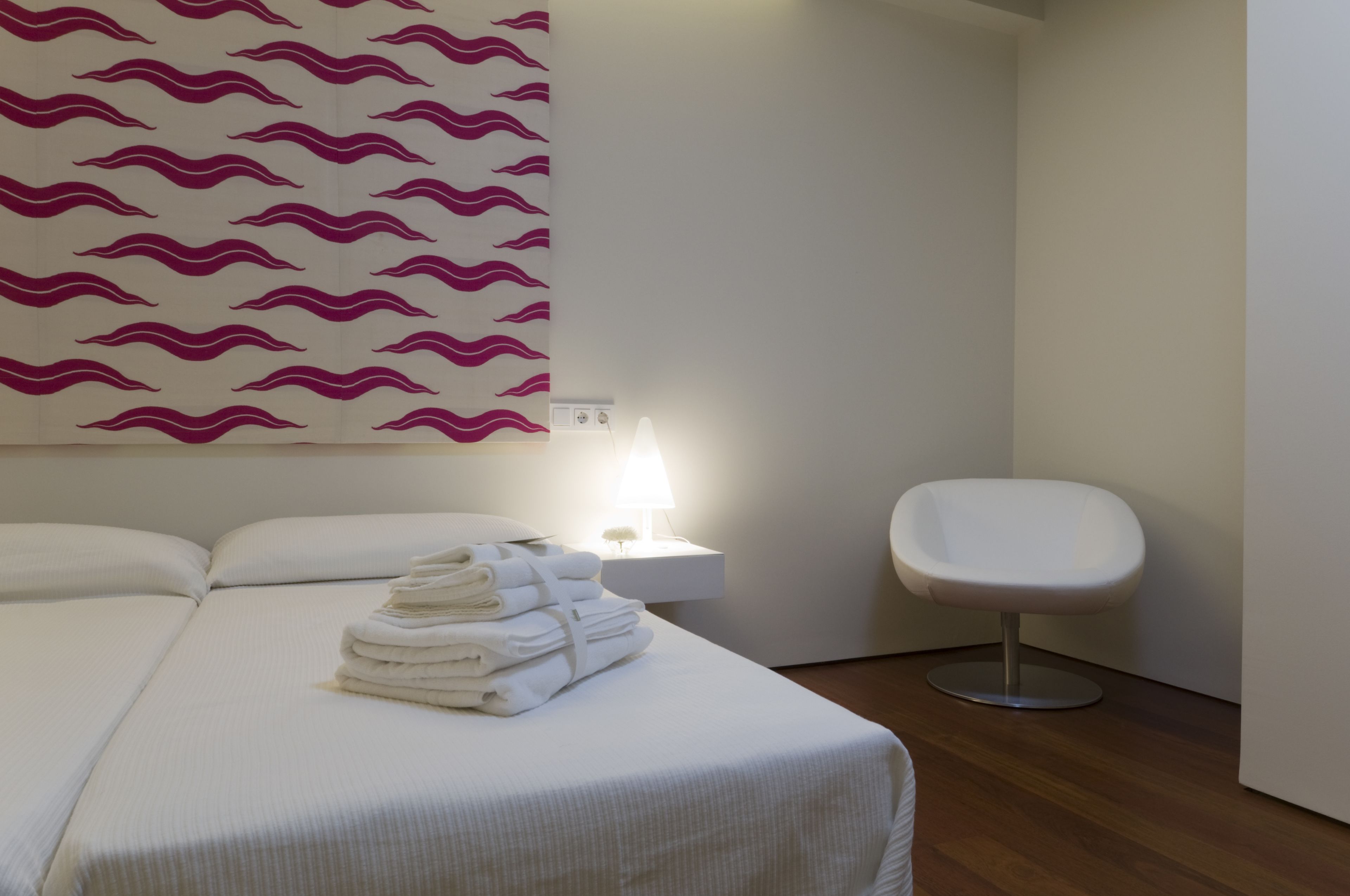 Une chambre d’hôtel avec un lit, une chaise et un mur orné d’un motif ondulé.