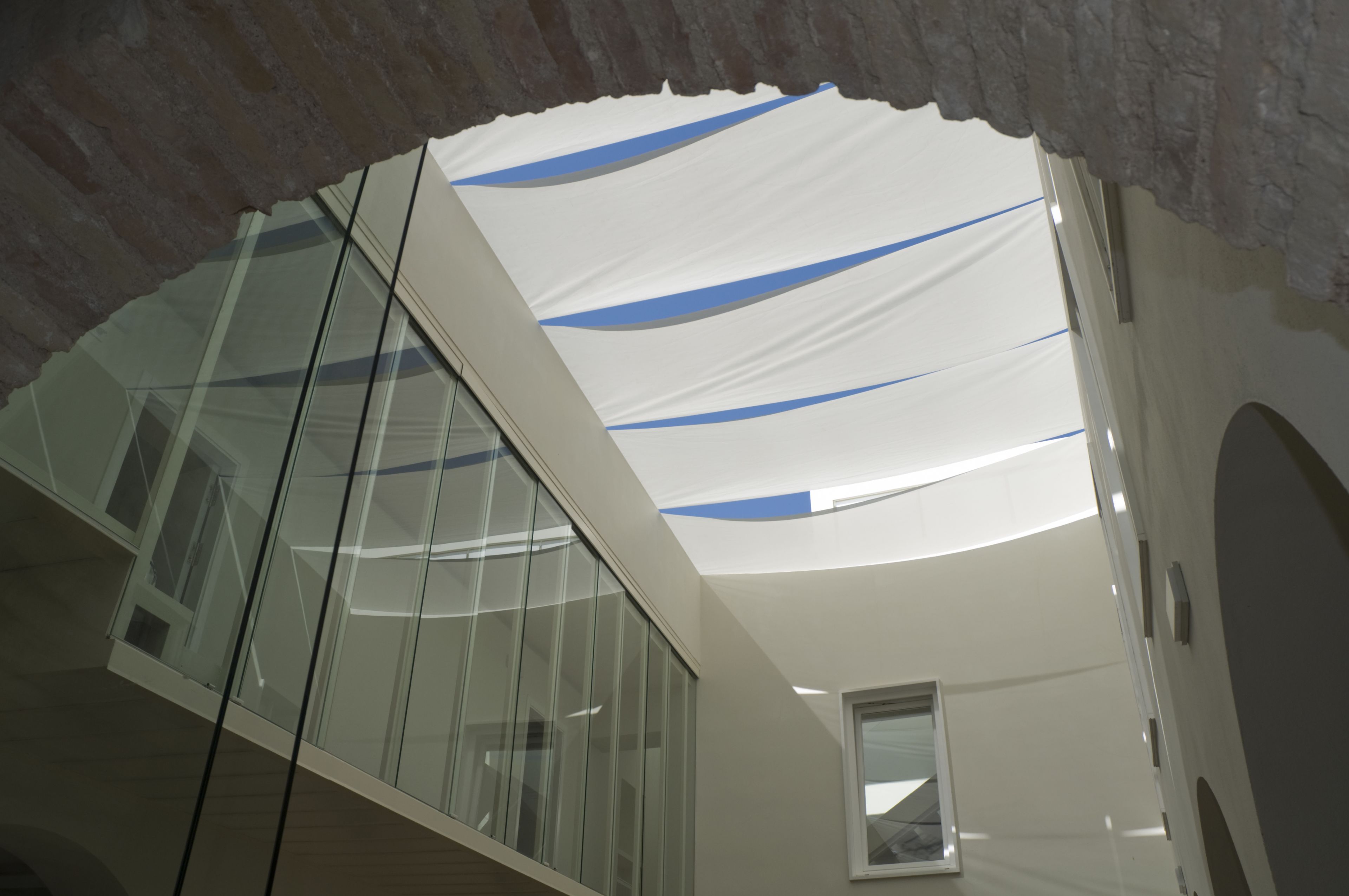 A modern interior with a glass railing, a white ceiling with blue accents, and a small window.