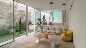 A modern living room with a large glass door leading to an outdoor area, a sofa, two white chairs, a coffee table, and a hanging light fixture. - Hotel Viento10 (Córdoba)