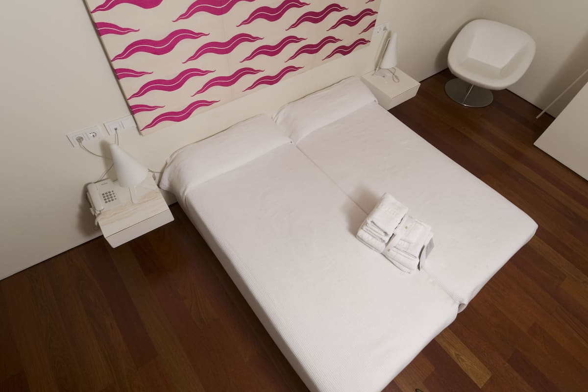 Una habitación de hotel con una cama, un teléfono blanco y una pared con un diseño ondulado color rosa.