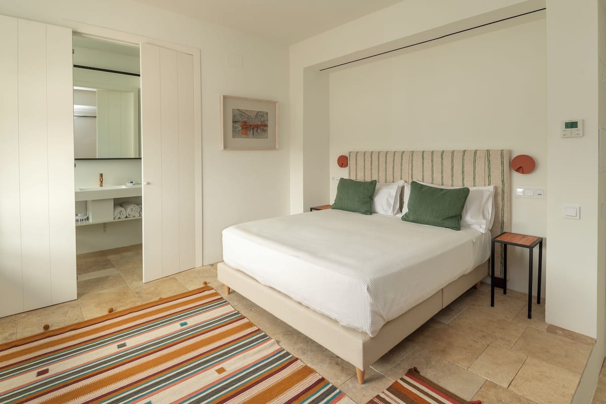 Un dormitorio con una cama, una mesita de noche, un espejo, un cuadro en la pared y una alfombra a rayas.