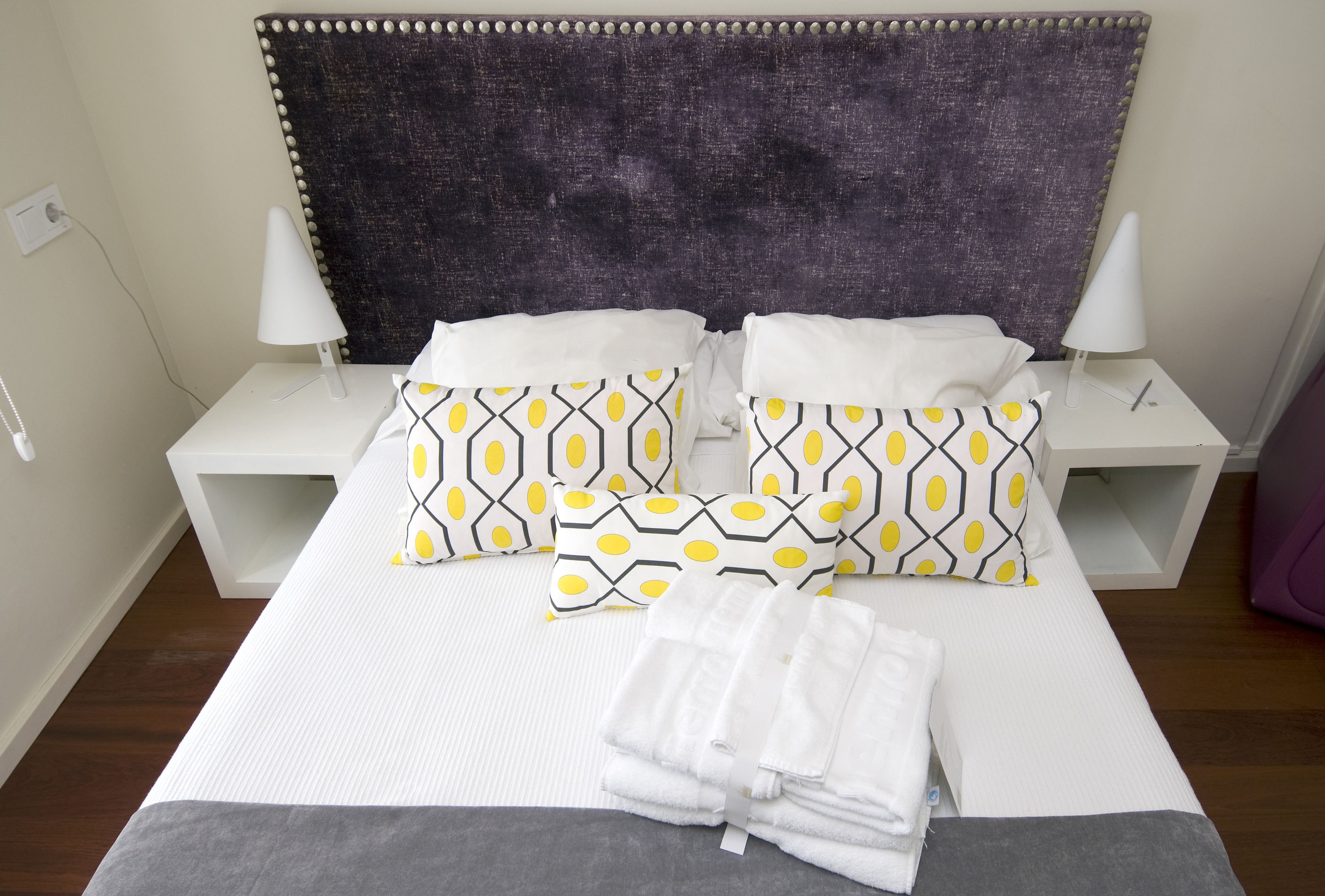 A neatly made bed with patterned pillows, white bedside tables, and a dark headboard.