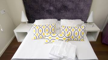A neatly made bed with patterned pillows, white bedside tables, and a dark headboard.