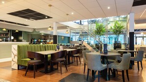 Un restaurante moderno con zona de bar, asientos y una escalera que lleva a un nivel superior.