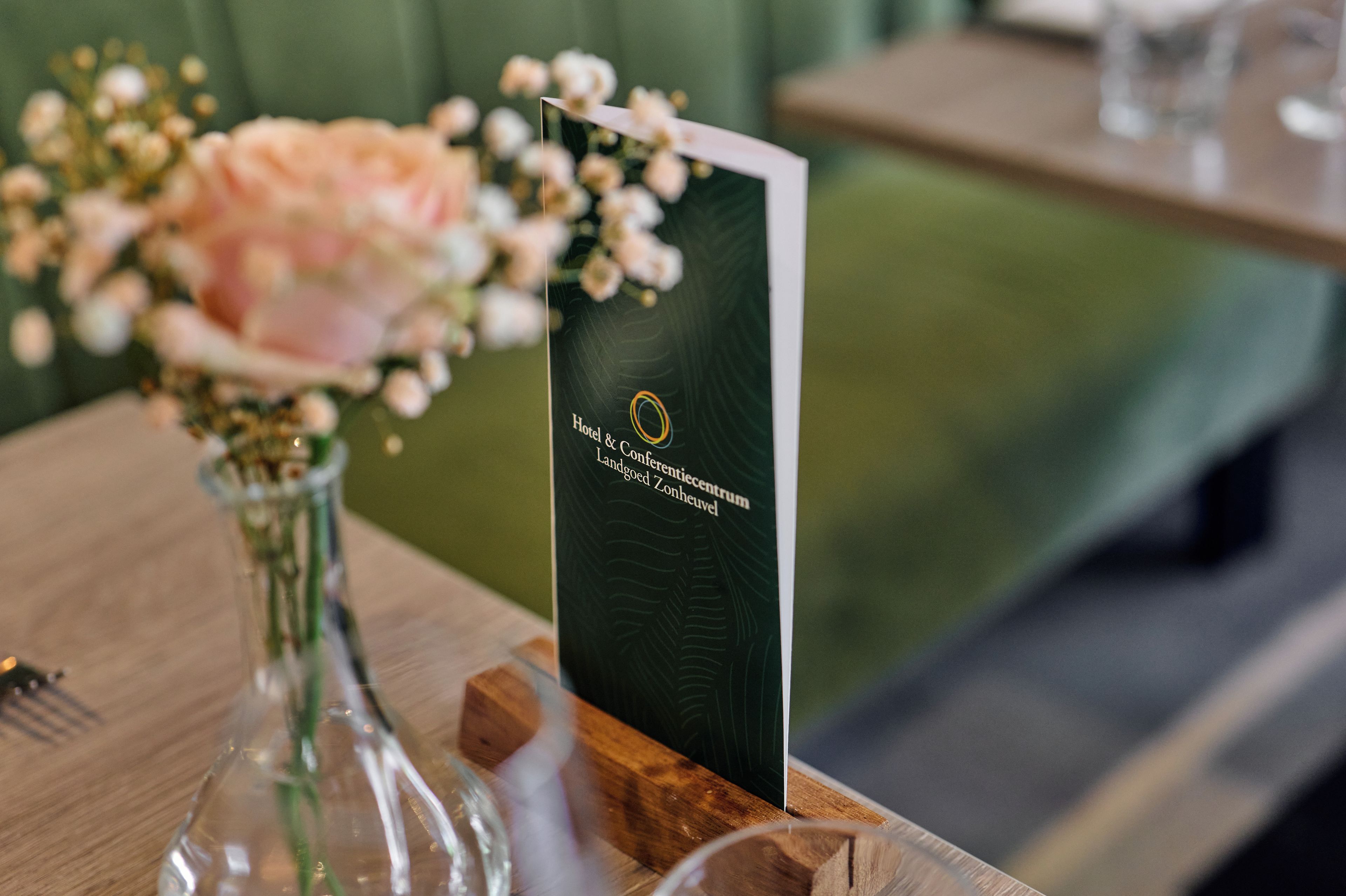 A table with a vase of flowers, a menu, and a wooden block.