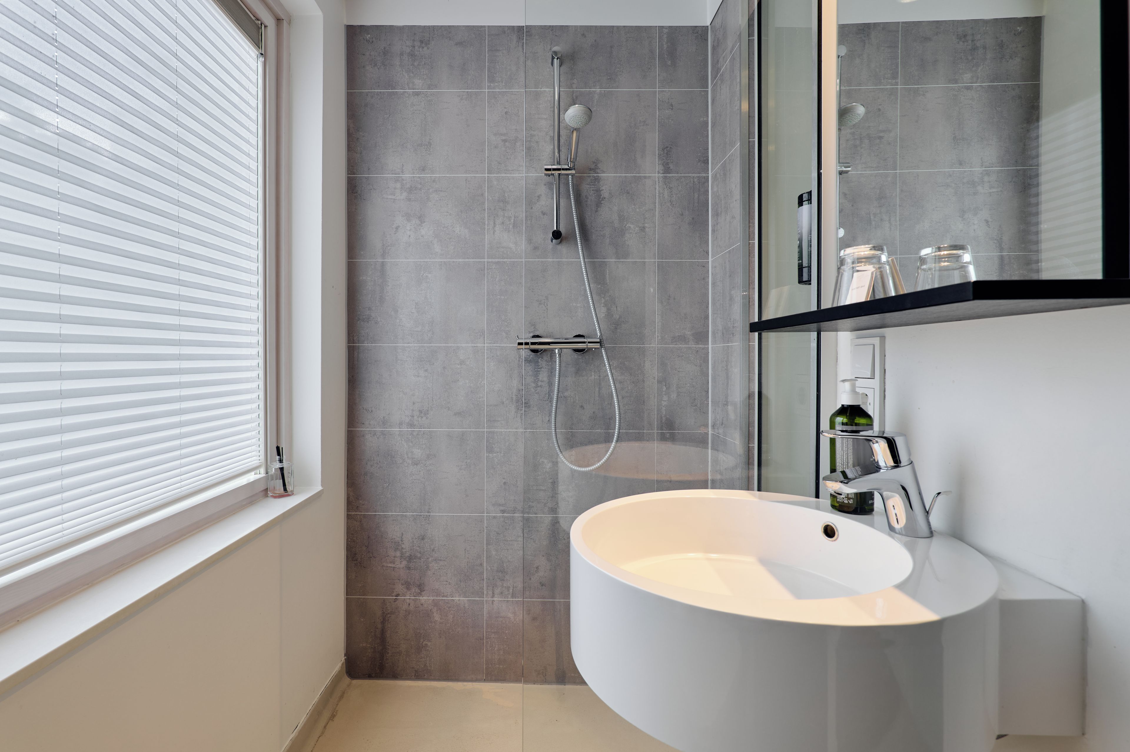 Un baño moderno con un lavamanos grande, una ducha con cabezal de ducha de mano y un espejo sobre el lavamanos.