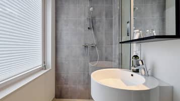 Un baño moderno con un lavamanos grande, una ducha con cabezal de ducha de mano y un espejo sobre el lavamanos.