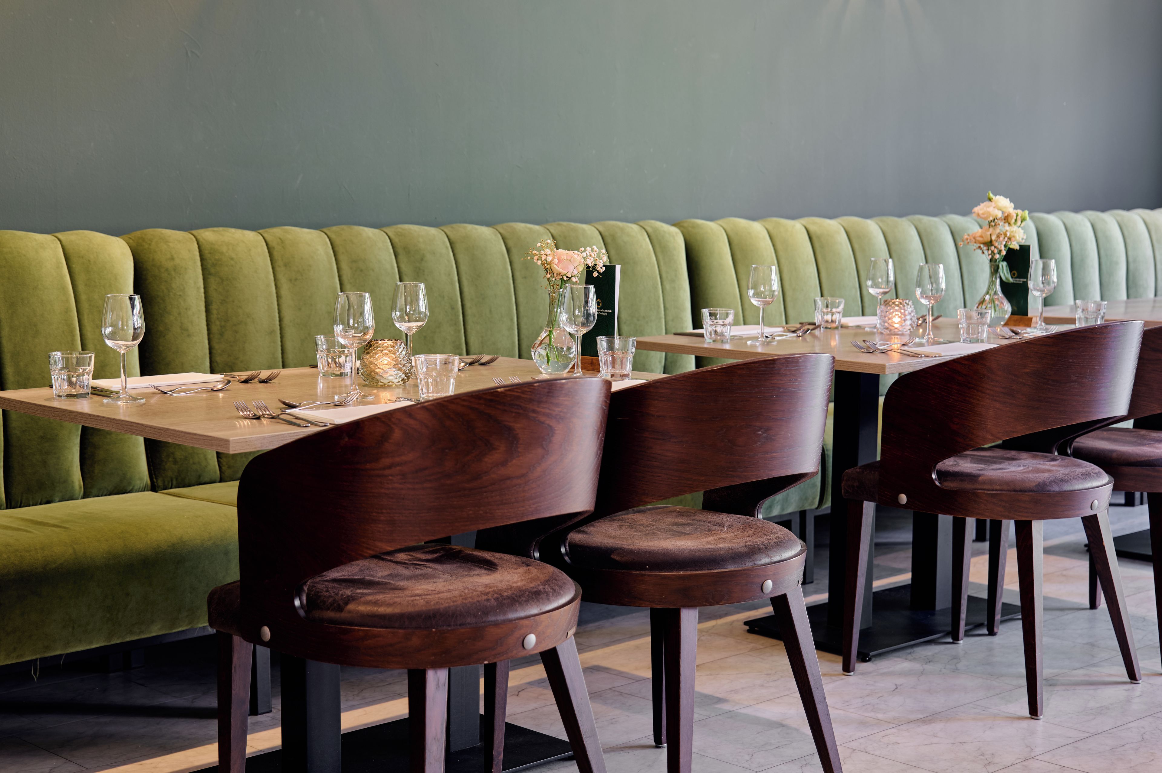 A restaurant with a green upholstered booth seating area and wooden tables with chairs.