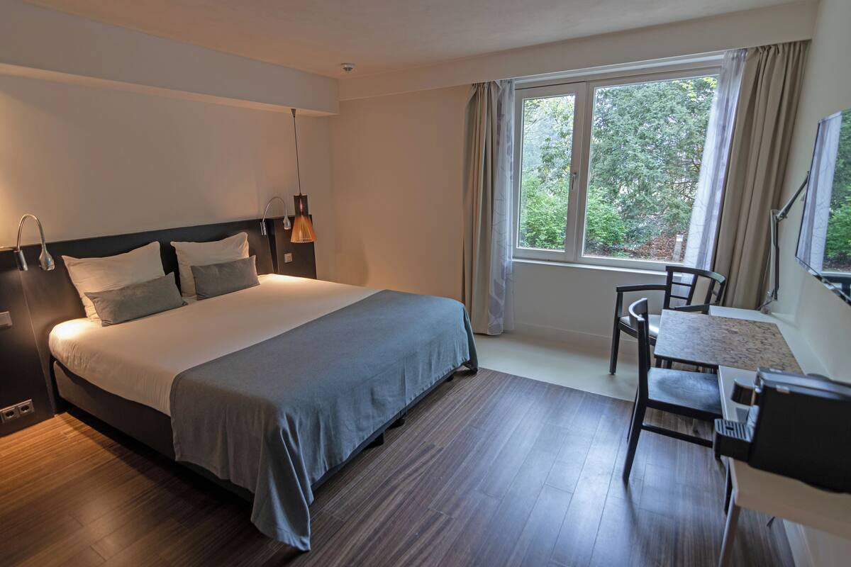 A modern hotel room with a large bed, a desk, and a window with curtains.