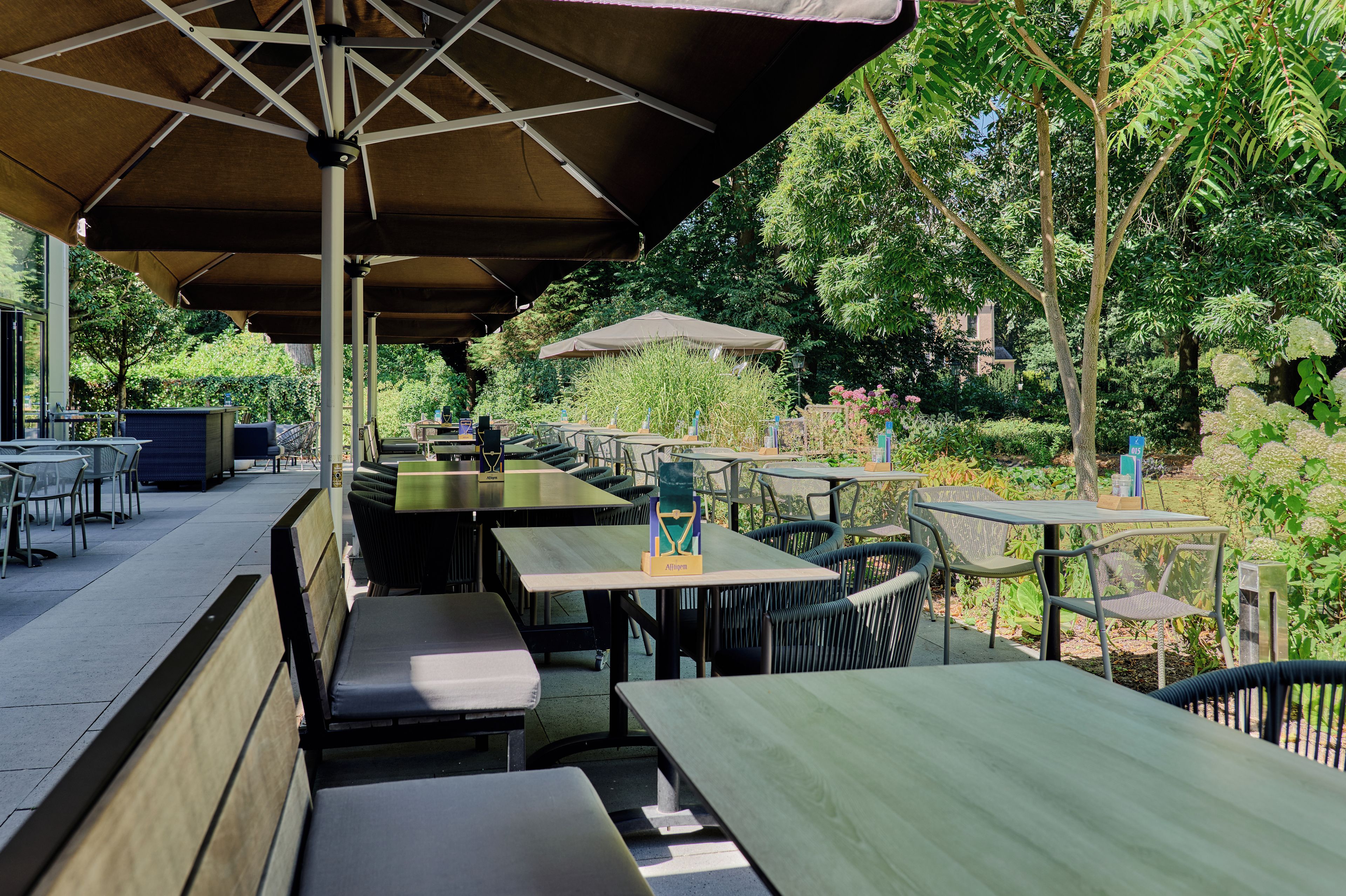 An outdoor seating area with tables and chairs, surrounded by greenery.
