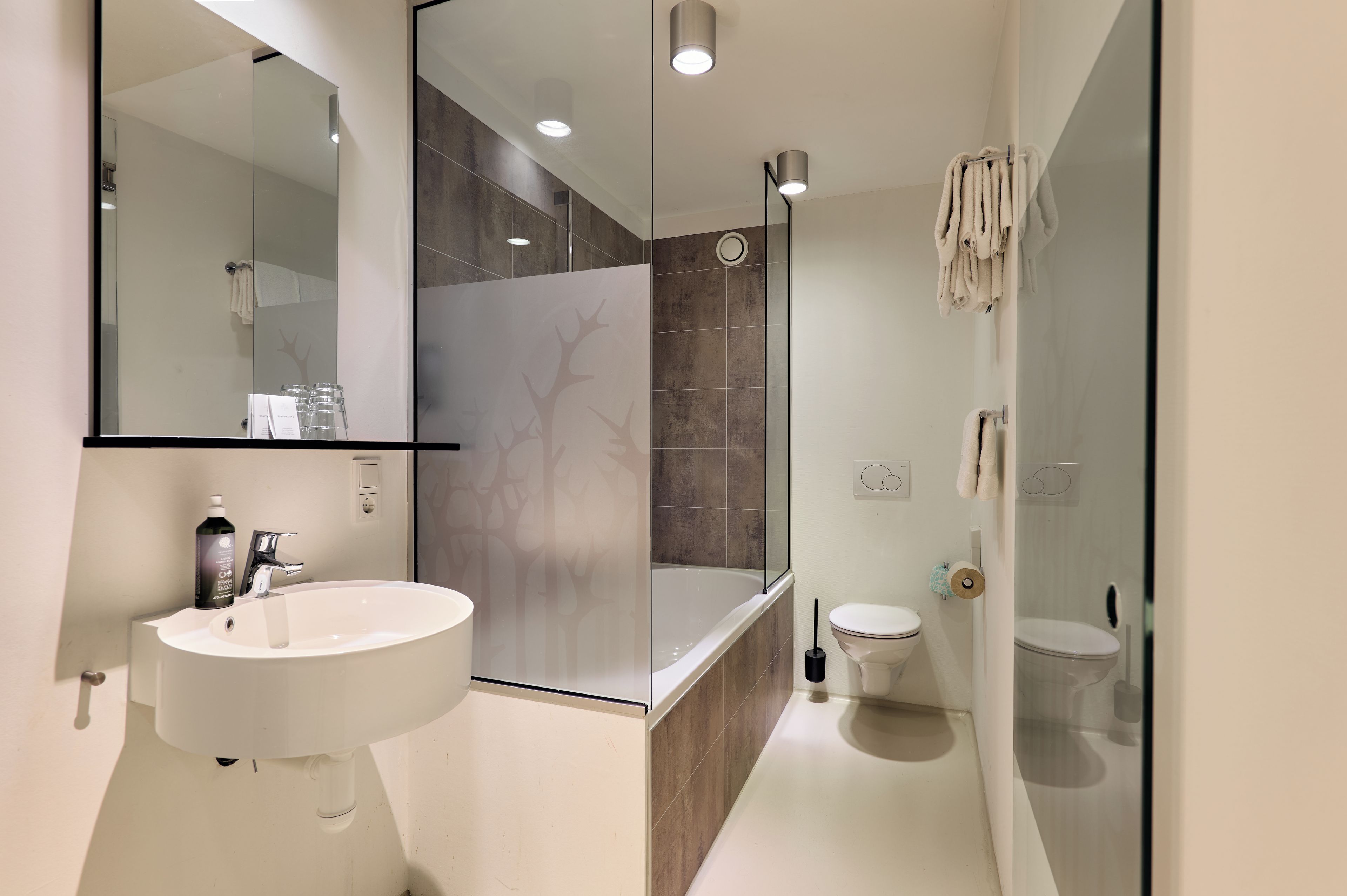 A modern bathroom with a large mirror, a sink, a bathtub, and a toilet.