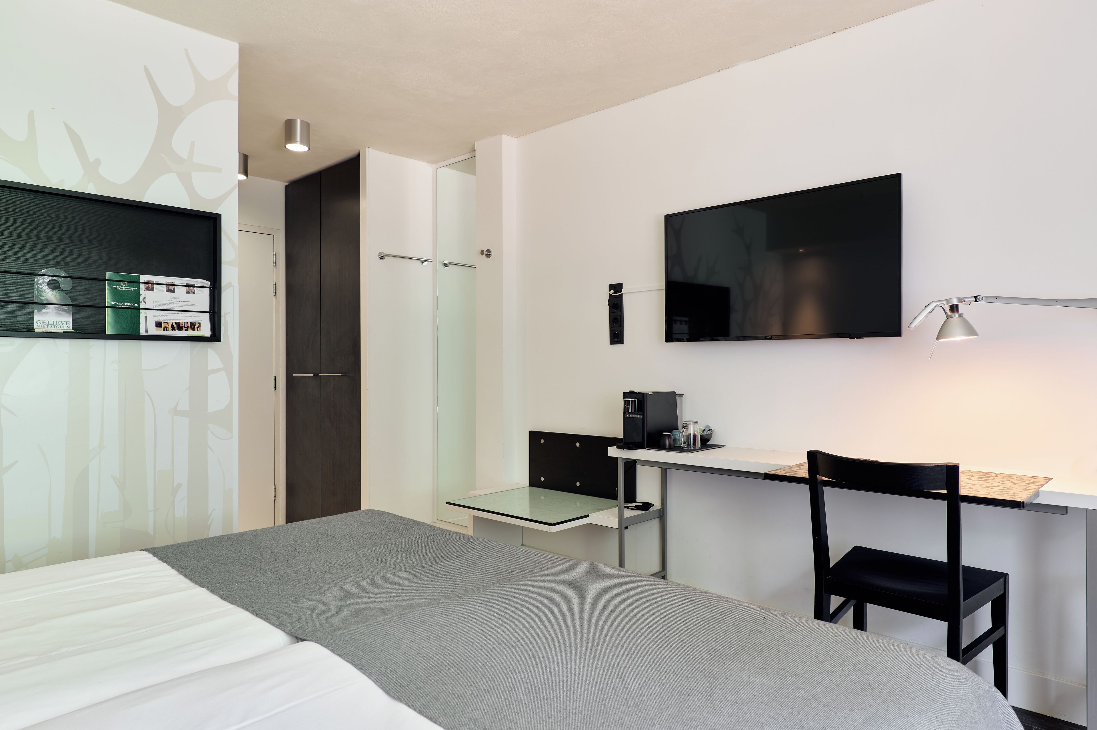 Een moderne hotelkamer met een bed, bureau, stoel en een flatscreen televisie aan de wand.