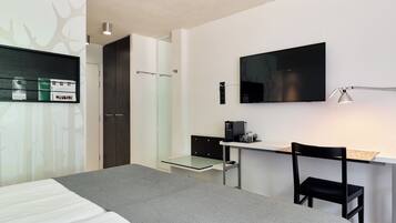 Een moderne hotelkamer met een bed, bureau, stoel en een flatscreen televisie aan de wand.