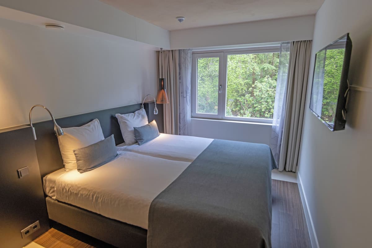 A double bed with a headboard, a bedside lamp, and a window with curtains.