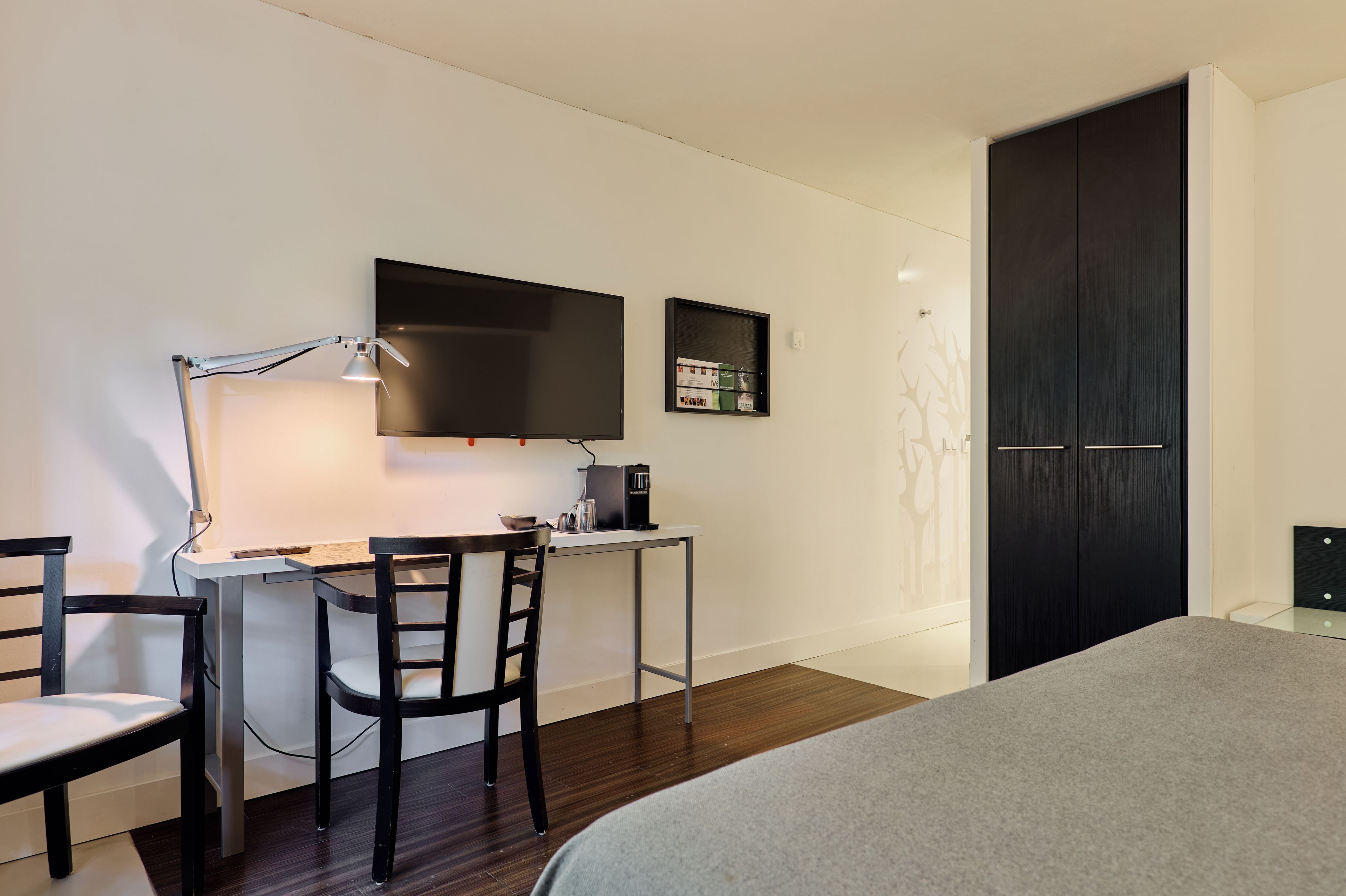 A modern bedroom with a bed, a desk with a chair, a TV, and a wardrobe.