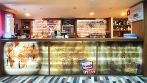 Una zona de bar con mostrador de madera, estantes con botellas y una pared con varias inscripciones y un mapa.