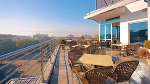 Una terraza en la azotea con mobiliario exterior, barandilla y vistas de la ciudad.