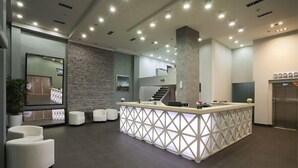 Un área de recepción moderna con un mostrador central, asientos, una escalera y un ascensor.