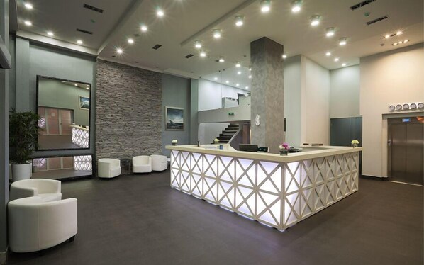 A modern reception area with a central counter, seating, a staircase, and an elevator.