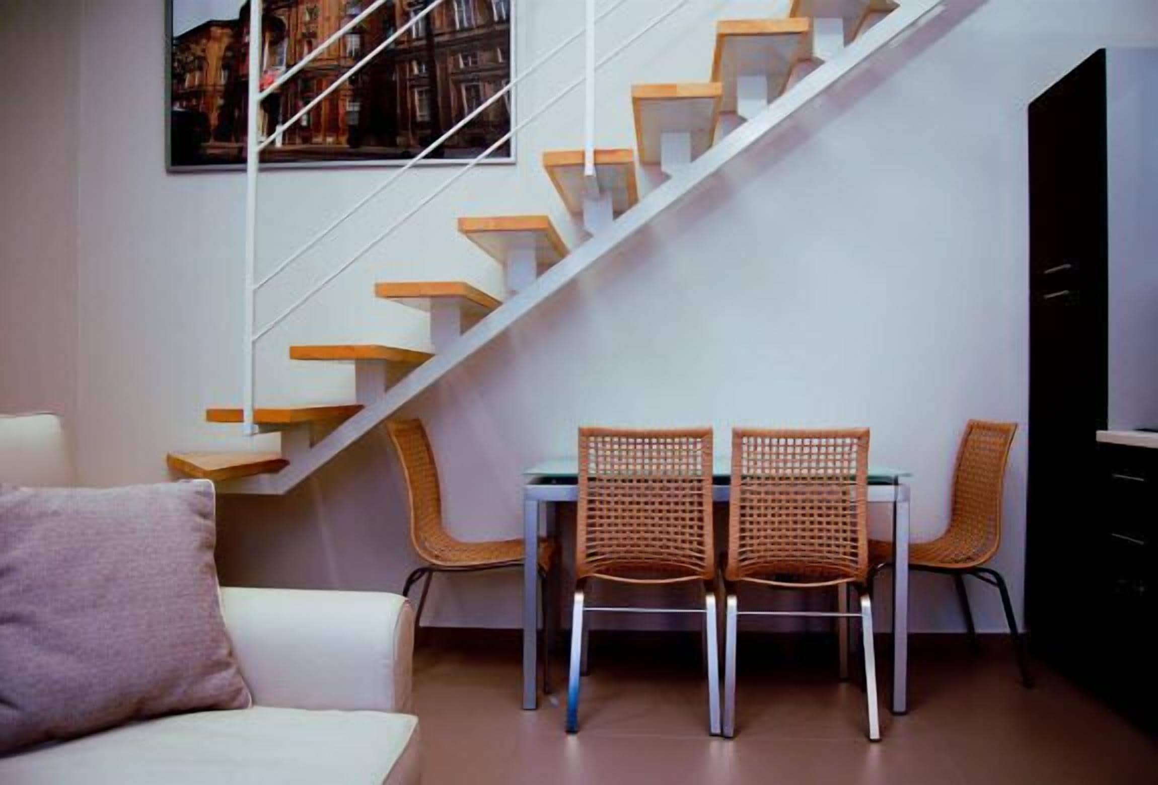 A modern interior with a staircase, a dining area with wicker chairs, and a white sofa.