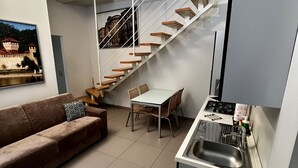 Une cuisine compacte équipée d’une cuisinière intégrée, d’un évier et d’un coin repas avec une table et des chaises. Un escalier mène à l’étage supérieur.