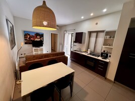 A modern kitchen with a dining area, a large pendant light, and a TV mounted on the wall.