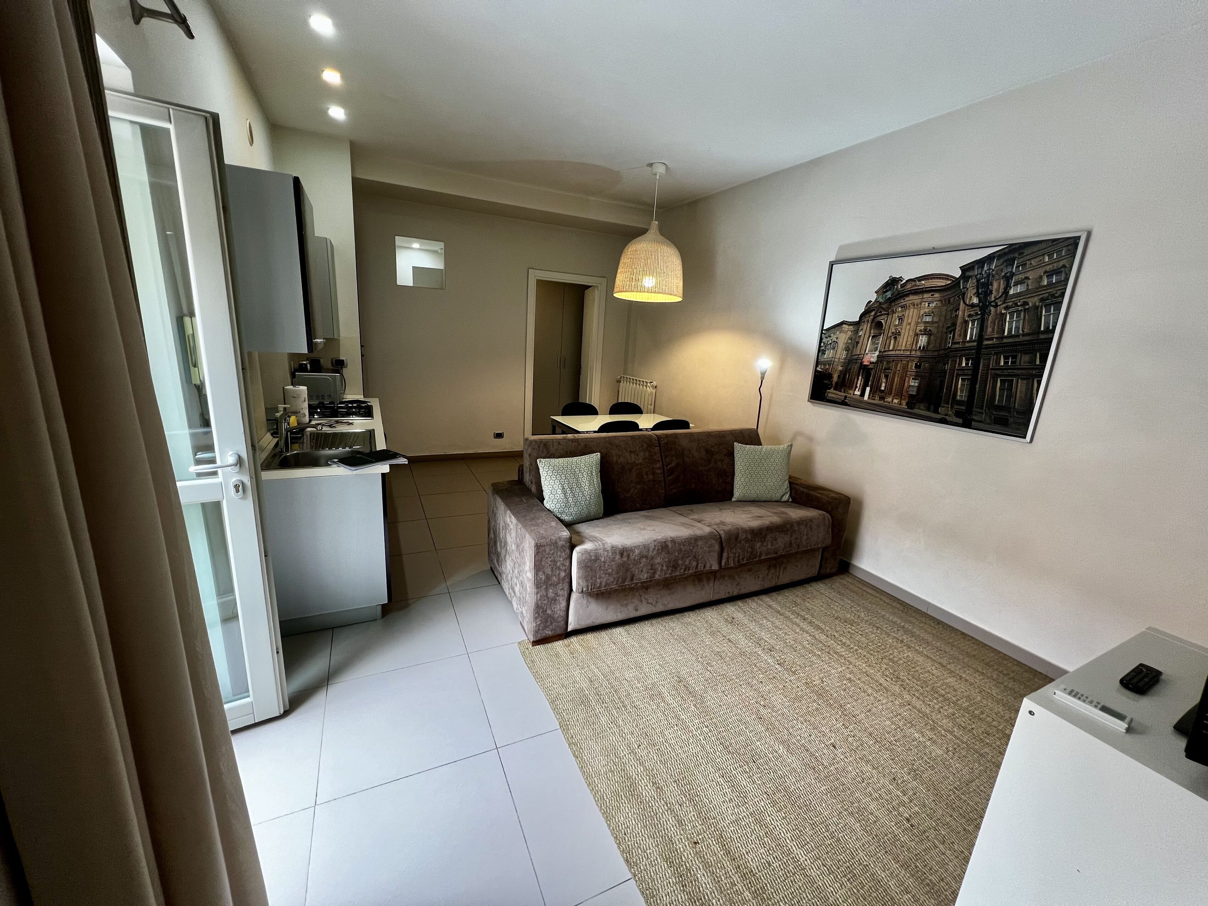 A modern apartment with a kitchenette, a sofa, a dining area, and a large window with a cityscape view.