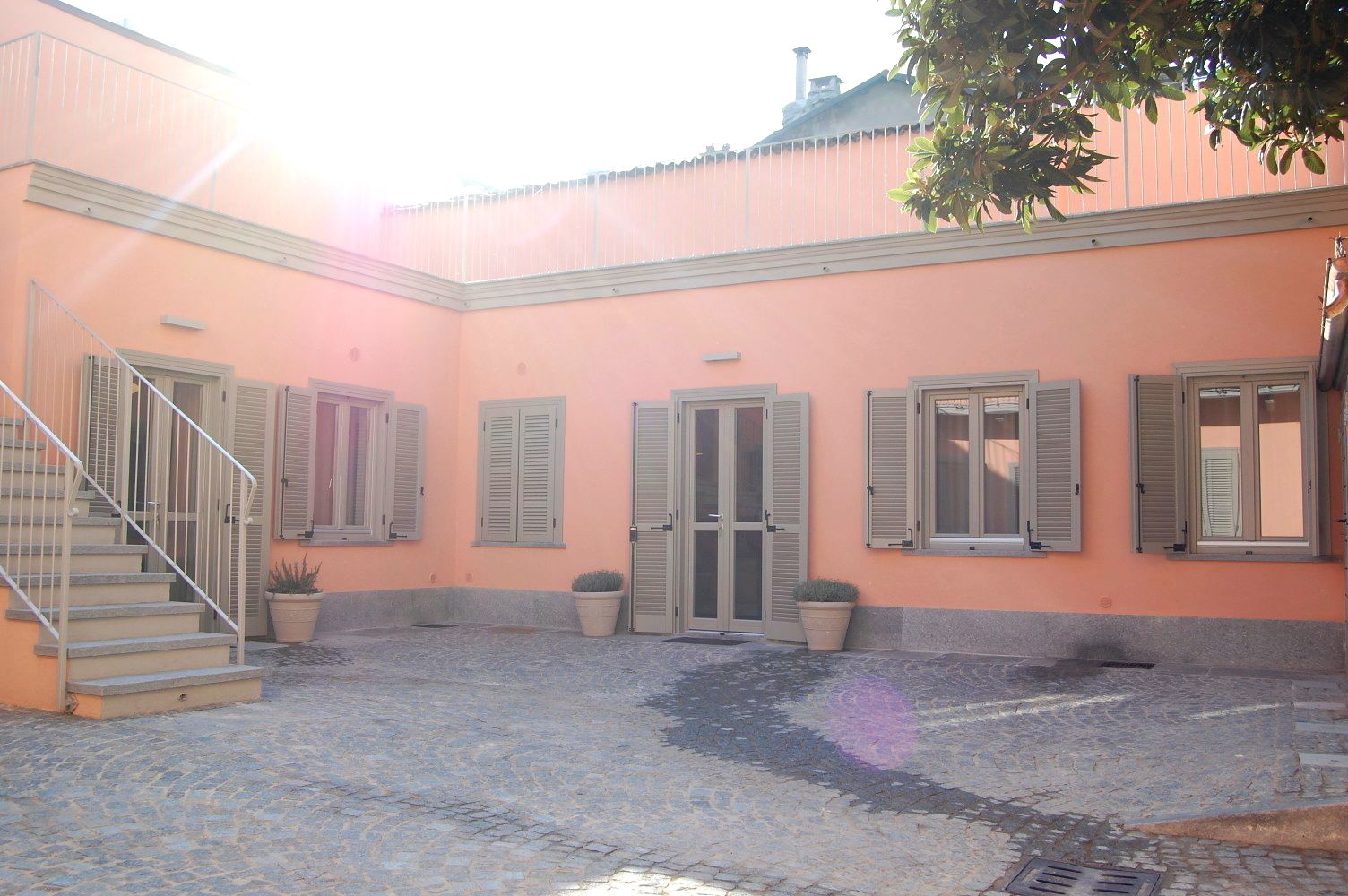 A courtyard with a cobblestone floor, a staircase, and a building with shutters and a door.