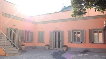 A courtyard with a cobblestone floor, a staircase, and a building with shutters and a door.