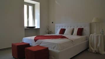 Une chambre à coucher avec un grand lit, deux poufs rouges, une fenêtre et une table de chevet avec une lampe.