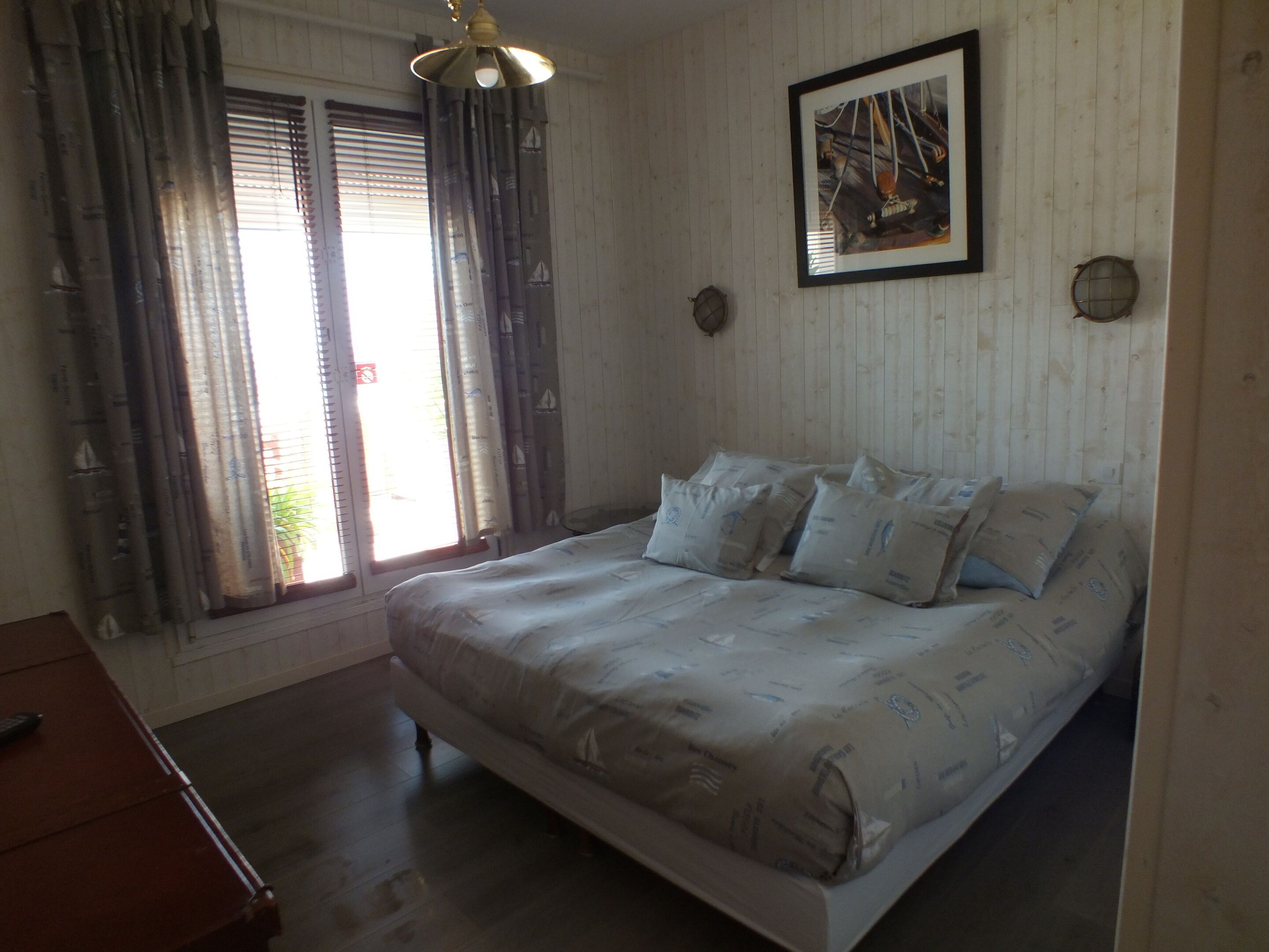 A bedroom with a bed, curtains, a painting, and a wooden floor.