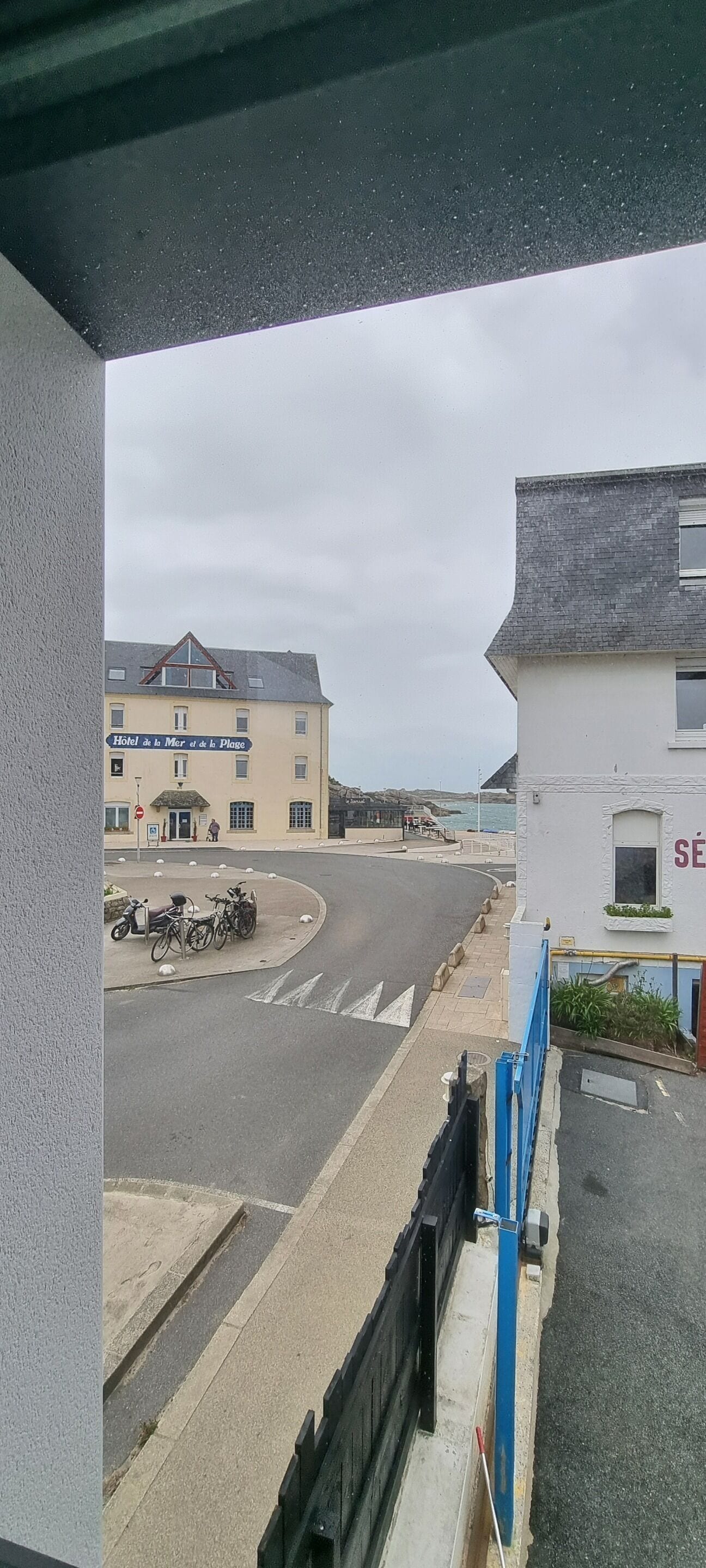 Een hotel met een bord waarop staat 'Hotel de la Mer et de la Plage', een parkeerplaats met fietsen en uitzicht op zee.