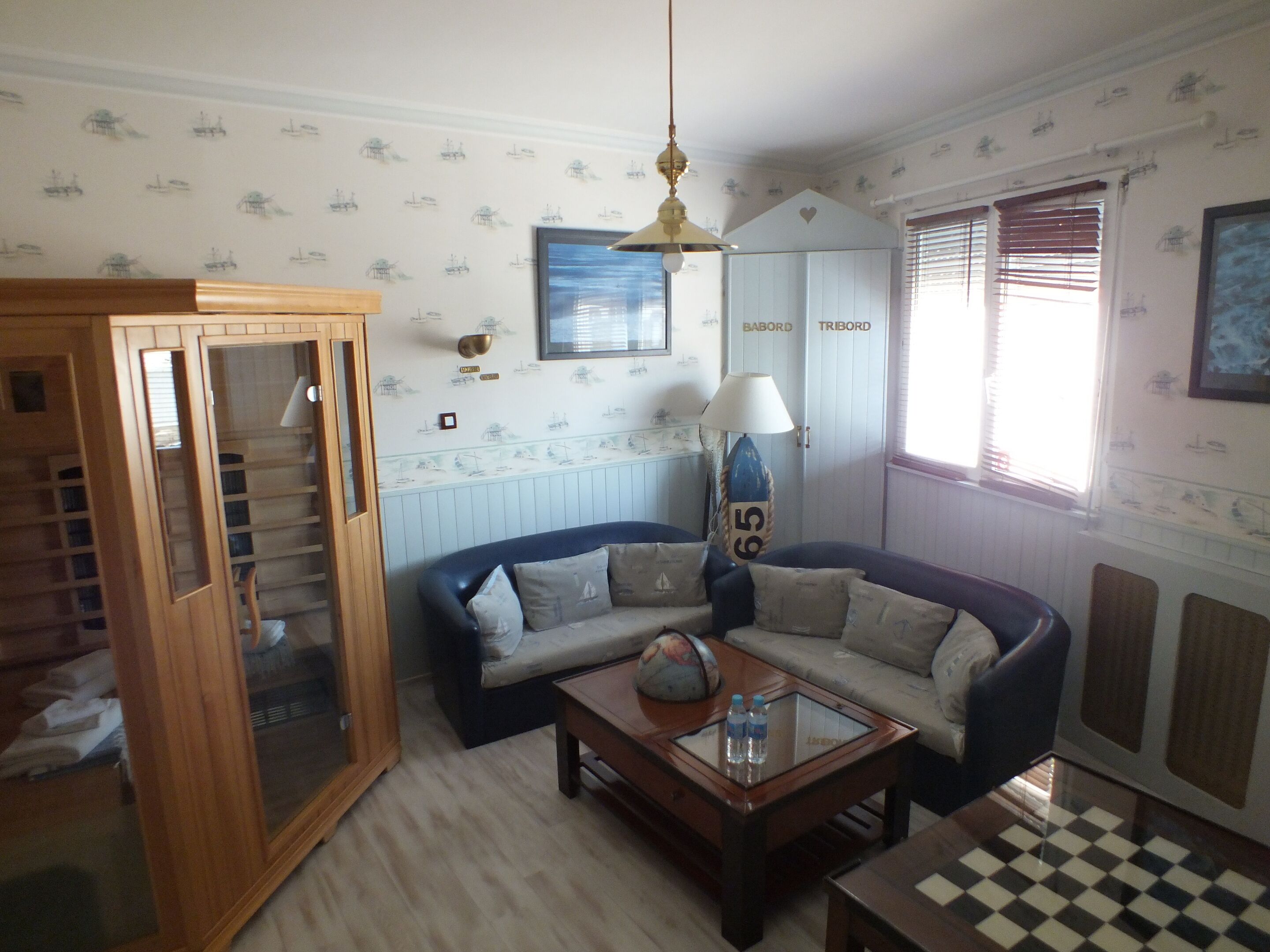 A room with a blue sofa, a wooden cabinet, a globe on a coffee table, and nautical-themed wallpaper.