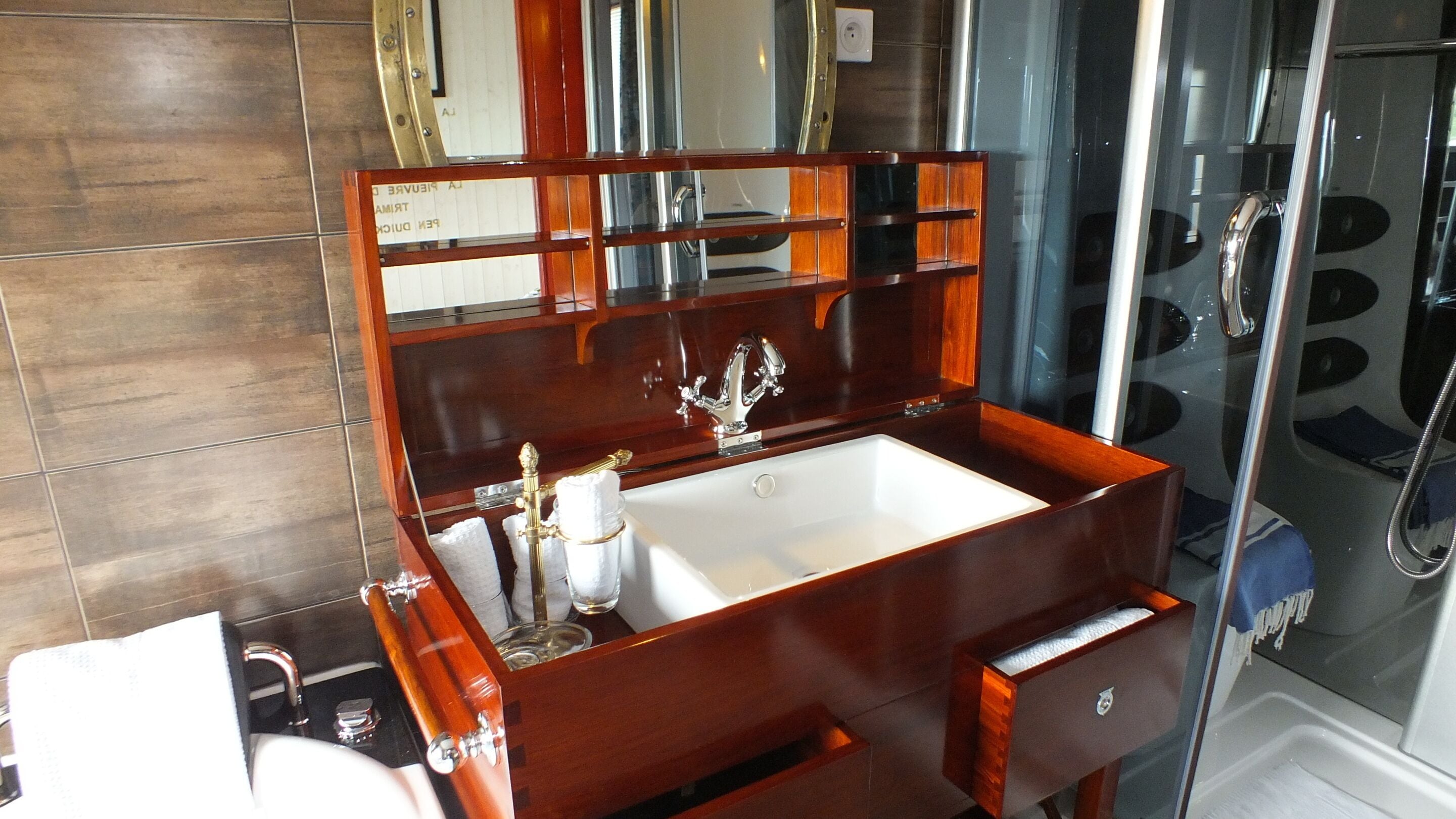 Une salle de bain avec un meuble-lavabo en bois, un lavabo blanc et une cabine de douche en verre.