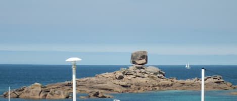 A rocky island with a unique rock formation in the center, surrounded by boats and a clear blue sea.