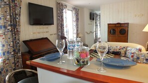 Habitación de hotel con cama, televisor, una mesa con vasos y botellas de agua, y cortinas con motivos náuticos.