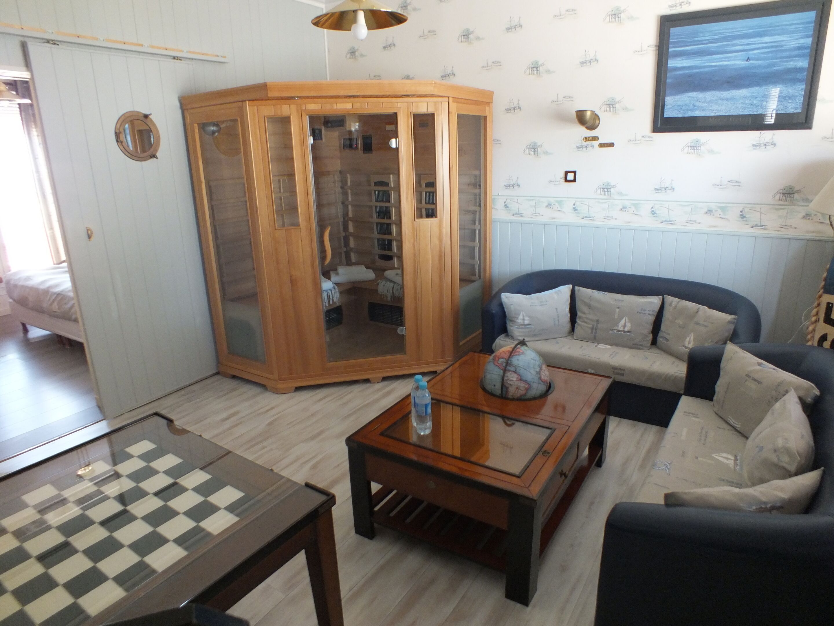 A room with a wooden cabinet, a sofa, a table with a globe, and a television on the wall.