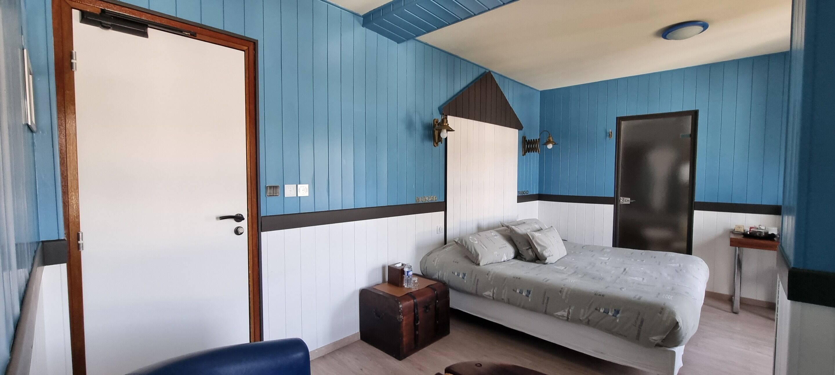 A bedroom with a bed, a bedside table, a chair, a suitcase, and a door.