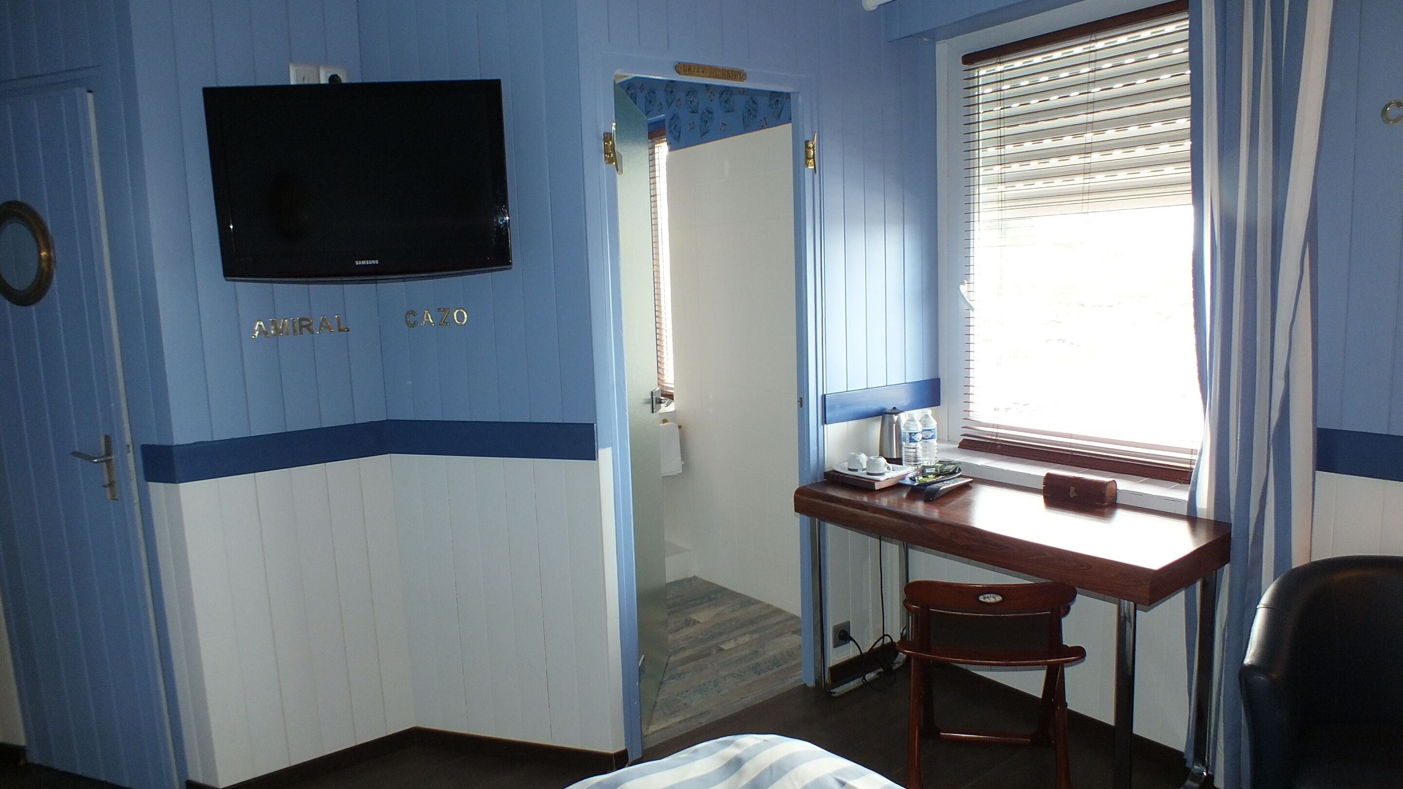 Ein Zimmer mit einem Bett, einem Schreibtisch mit Stuhl, einem Fernseher und einem Fenster mit Jalousien.