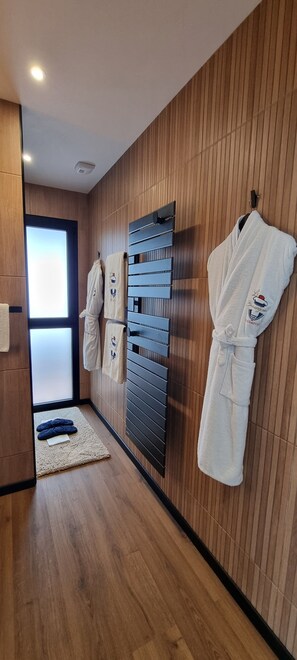 A modern bathroom with wooden paneling, a towel rack with multiple towels, a heated towel rail, and a wooden floor. - Le Beauséjour (Tregastel)