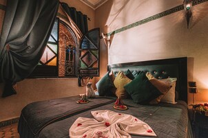 Una cama con cabecera oscura, una ventana con ornamentación de hierro y una lámpara fijada a la pared.