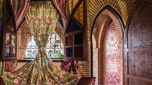 Une pièce avec des rideaux à motifs floraux, une fenêtre ornée de barreaux en fer et une porte en bois aux sculptures complexes.