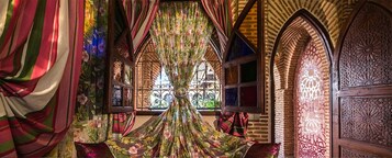 Una habitación con cortina floral, ventana con rejas de hierro y puerta de madera con tallado intrincado.