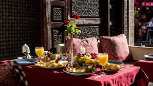 Une table mise pour le petit-déjeuner, avec des fruits, du pain et du jus, ainsi qu’un vase décoratif et une rose.