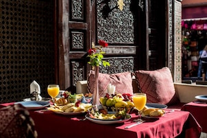Una mesa dispuesta con desayuno que incluye frutas, pan y jugo, con un jarrón decorativo y una rosa.