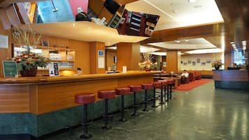 A hotel lobby with a reception desk, bar stools, seating area, and a large mirror.